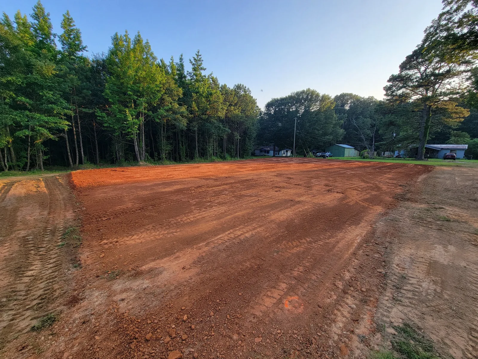 Red clay house pad graded flat with the treeline behind