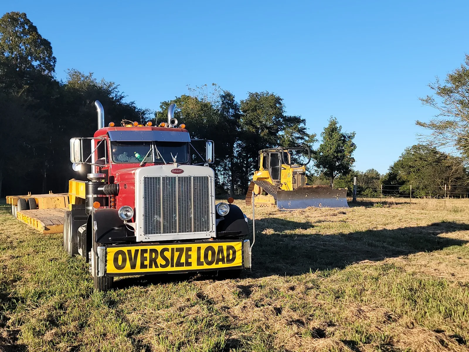 Trackhoe chained down on the lowboy with the oversize load banner on the truck