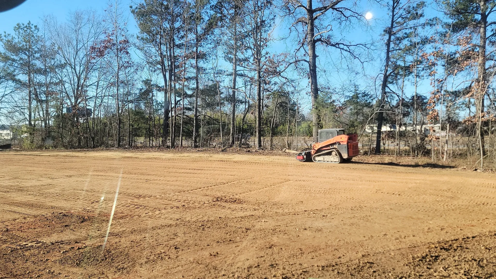 Wide graded site with the skid steer finishing the grade